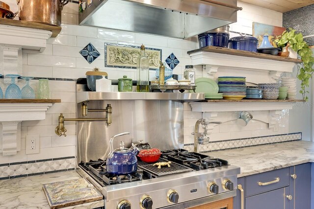 kitchen with backsplash, light stone counters, range hood, and stainless steel range oven