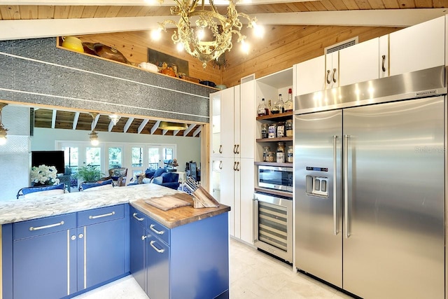 kitchen featuring white cabinets, built in appliances, vaulted ceiling with beams, blue cabinetry, and butcher block countertops