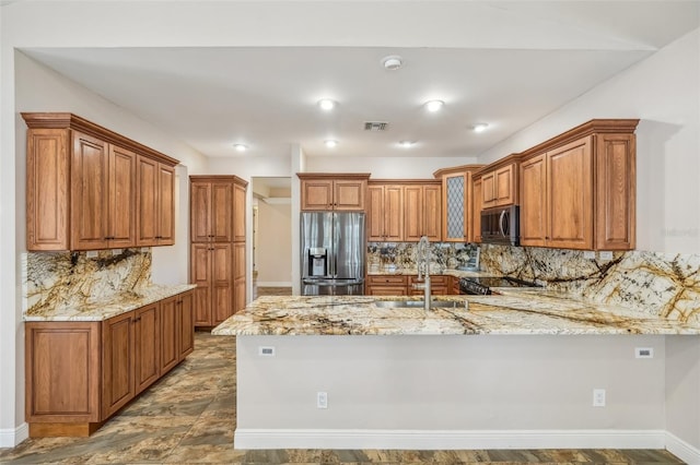 kitchen with appliances with stainless steel finishes, kitchen peninsula, light stone counters, decorative backsplash, and sink