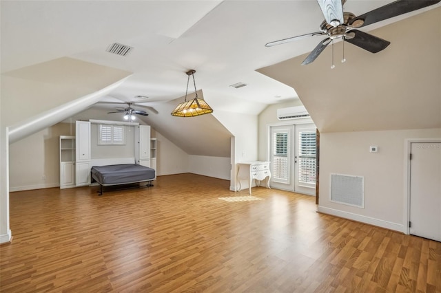 additional living space featuring a wall mounted AC, vaulted ceiling, french doors, light wood-type flooring, and ceiling fan