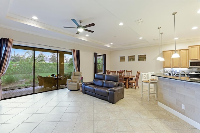 tiled living room with a raised ceiling, ceiling fan, crown molding, and sink