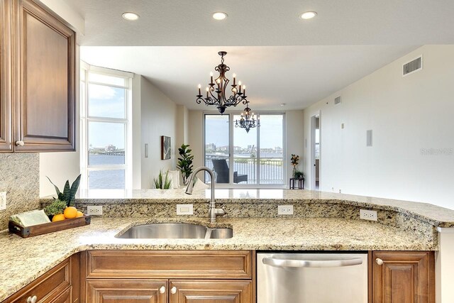 kitchen with light stone countertops, dishwasher, decorative backsplash, sink, and a water view