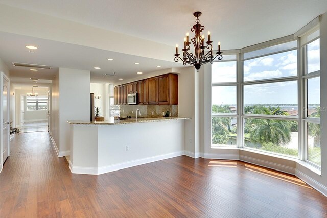 kitchen with a healthy amount of sunlight, an inviting chandelier, backsplash, kitchen peninsula, and light stone counters