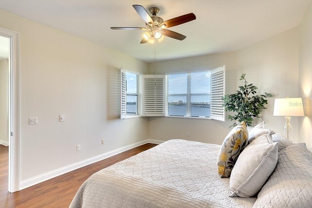 bedroom featuring dark wood-type flooring, ceiling fan, and a water view