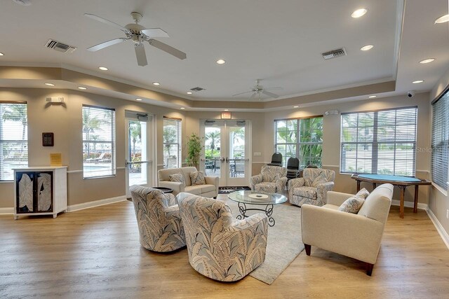 living room with a raised ceiling, french doors, crown molding, and light hardwood / wood-style floors