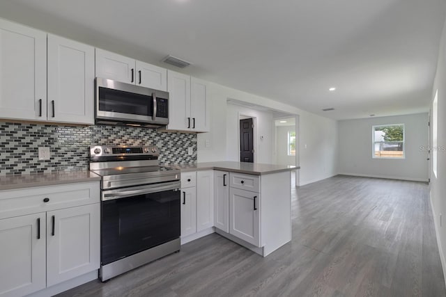 kitchen featuring appliances with stainless steel finishes, kitchen peninsula, hardwood / wood-style flooring, decorative backsplash, and white cabinets