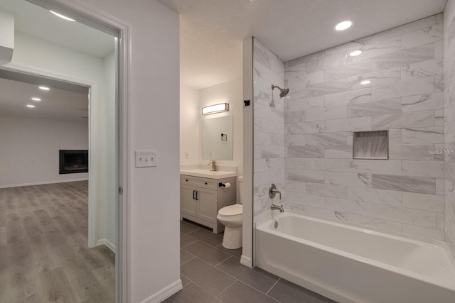 full bathroom with toilet, tiled shower / bath, vanity, and a fireplace