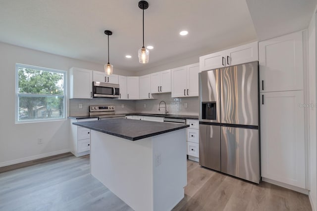 kitchen featuring appliances with stainless steel finishes, decorative light fixtures, white cabinetry, sink, and light hardwood / wood-style floors