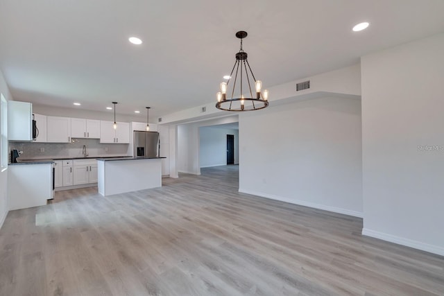 kitchen with stainless steel refrigerator with ice dispenser, sink, tasteful backsplash, hanging light fixtures, and white cabinets