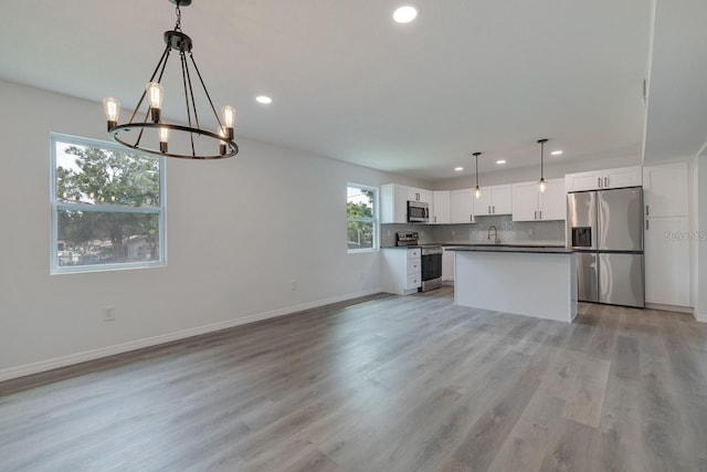 kitchen with sink, light hardwood / wood-style flooring, hanging light fixtures, stainless steel appliances, and white cabinets