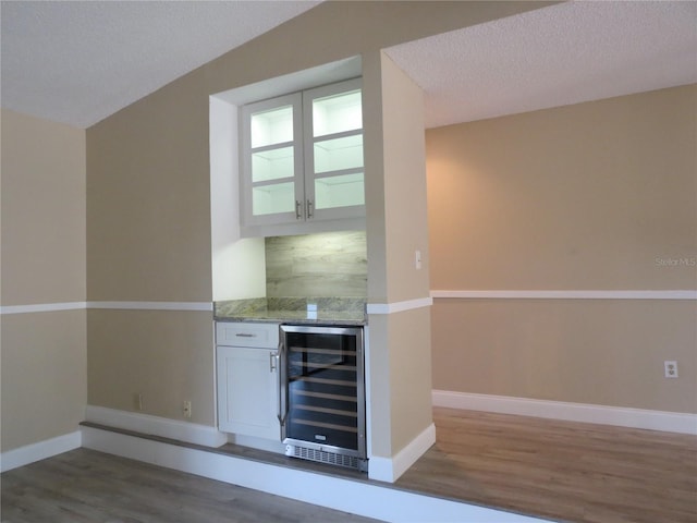 bar featuring white cabinets, light stone countertops, a textured ceiling, and beverage cooler