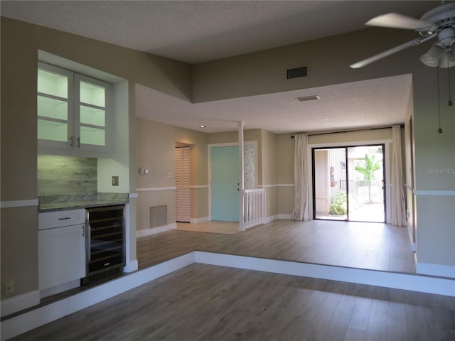 kitchen with wine cooler, a textured ceiling, ceiling fan, hardwood / wood-style flooring, and white cabinetry