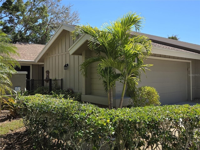 view of side of home featuring a garage, board and batten siding, and roof with shingles