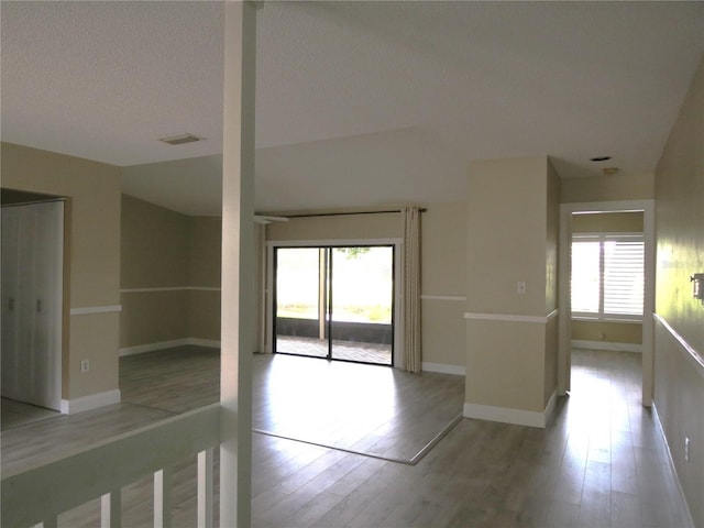 spare room featuring a wealth of natural light, a textured ceiling, light wood-type flooring, and baseboards