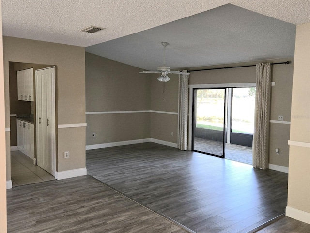 empty room featuring a ceiling fan, baseboards, visible vents, dark wood-type flooring, and a textured ceiling