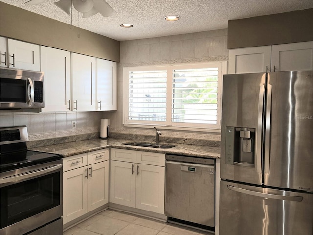 kitchen with light tile patterned floors, a sink, appliances with stainless steel finishes, a textured ceiling, and white cabinetry