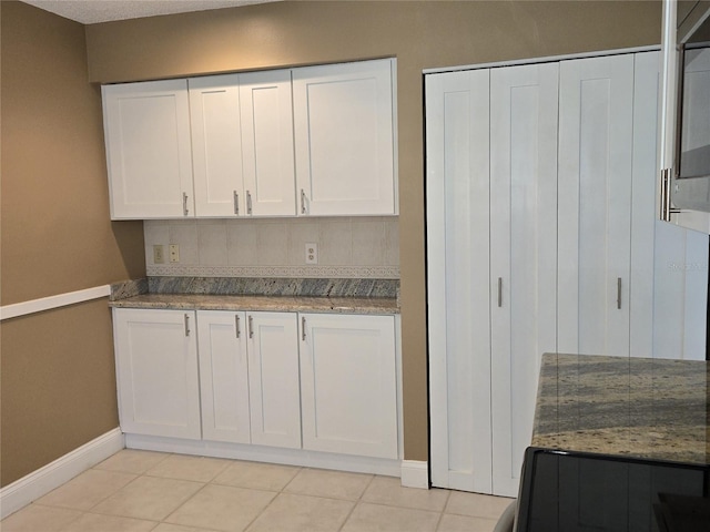 kitchen featuring white cabinetry, light tile patterned floors, light stone countertops, and baseboards