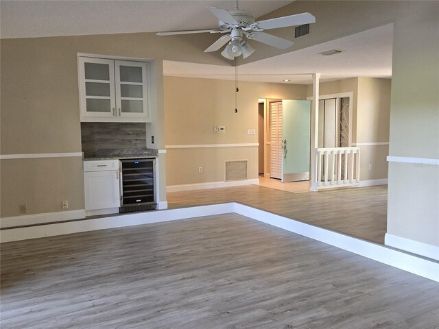 interior space with wood finished floors, beverage cooler, visible vents, vaulted ceiling, and a dry bar