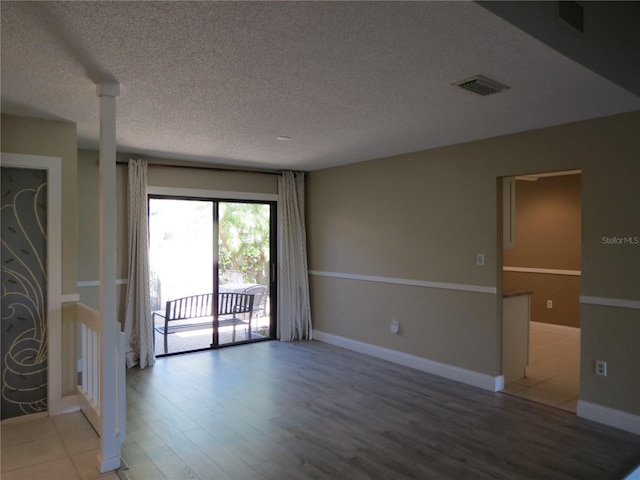 empty room with visible vents, a textured ceiling, baseboards, and wood finished floors