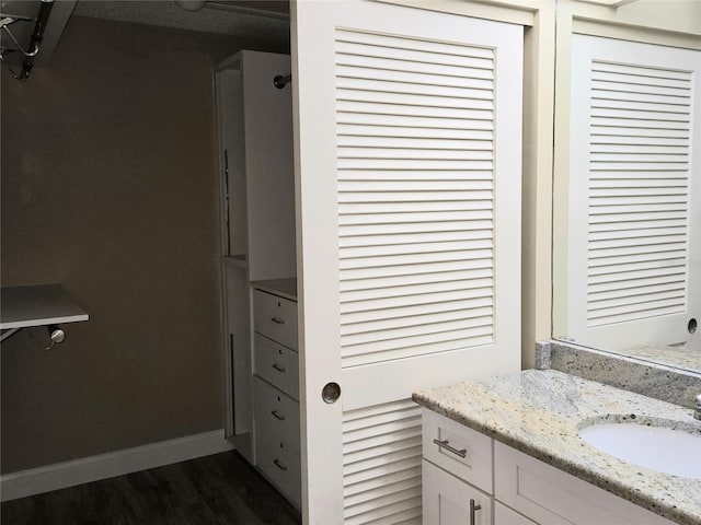 bathroom with a closet, baseboards, wood finished floors, and vanity