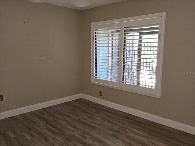 unfurnished room featuring dark wood finished floors, a healthy amount of sunlight, and baseboards