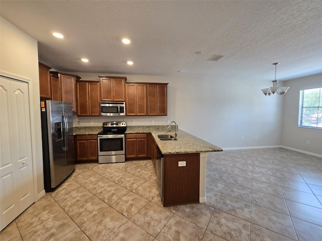 kitchen featuring sink, light stone counters, kitchen peninsula, decorative light fixtures, and appliances with stainless steel finishes