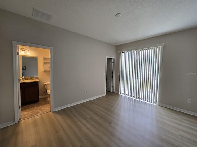 unfurnished bedroom featuring light hardwood / wood-style floors, a textured ceiling, and ensuite bath