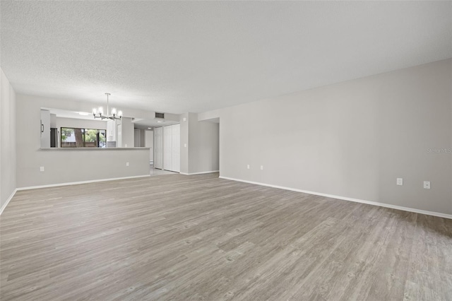 unfurnished living room with a chandelier, a textured ceiling, and light hardwood / wood-style flooring