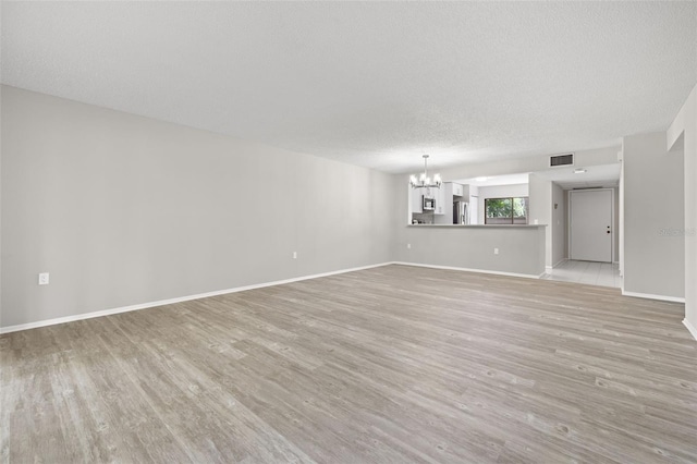 unfurnished living room featuring light hardwood / wood-style floors, a textured ceiling, and a notable chandelier