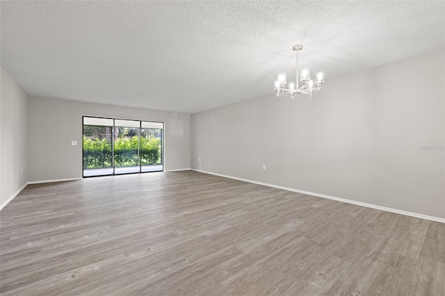 empty room featuring hardwood / wood-style floors, a textured ceiling, and an inviting chandelier