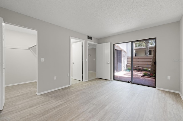 unfurnished bedroom featuring access to exterior, light wood-type flooring, a walk in closet, and a closet