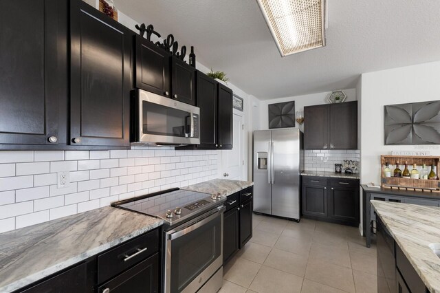 kitchen with appliances with stainless steel finishes, tasteful backsplash, light tile floors, and light stone counters