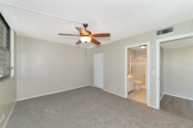 unfurnished bedroom with a textured ceiling, a closet, connected bathroom, carpet flooring, and ceiling fan