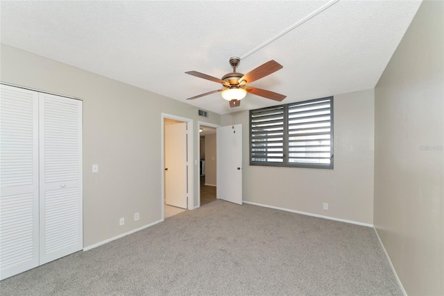 unfurnished bedroom with ceiling fan, a closet, light carpet, and a textured ceiling