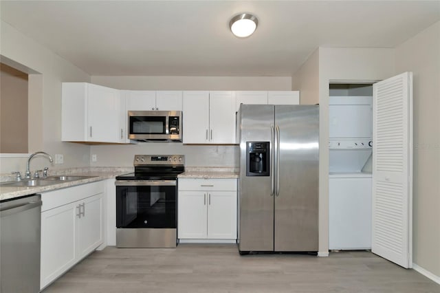 kitchen featuring stainless steel appliances, white cabinets, stacked washer and clothes dryer, and sink