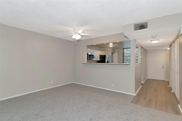 empty room featuring ceiling fan, light carpet, and a textured ceiling