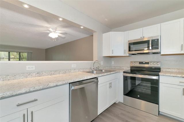 kitchen with light wood-type flooring, sink, light stone counters, appliances with stainless steel finishes, and white cabinets