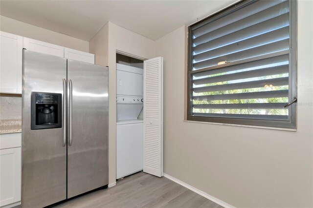 kitchen with white cabinetry, stacked washer / drying machine, stainless steel fridge, and a wealth of natural light