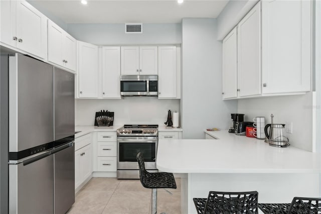 kitchen with light tile patterned floors, white cabinetry, kitchen peninsula, and appliances with stainless steel finishes