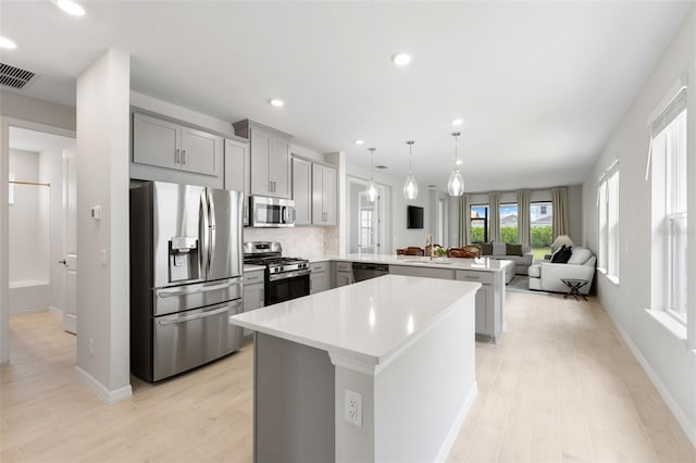 kitchen with sink, a center island, kitchen peninsula, decorative light fixtures, and appliances with stainless steel finishes