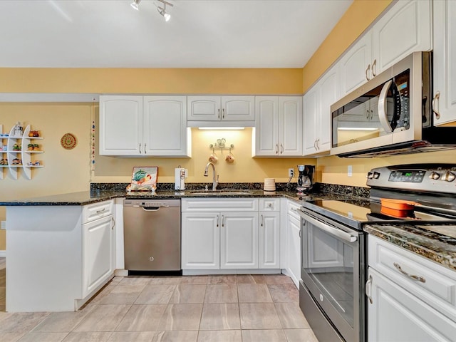 kitchen with white cabinets, appliances with stainless steel finishes, dark stone countertops, and sink