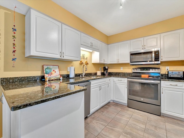 kitchen with white cabinetry, sink, kitchen peninsula, dark stone countertops, and appliances with stainless steel finishes