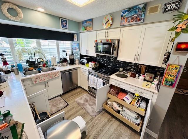 kitchen featuring stainless steel appliances, white cabinets, a textured ceiling, and light hardwood / wood-style flooring