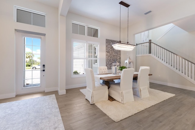 dining space featuring a towering ceiling, wood-type flooring, and an inviting chandelier