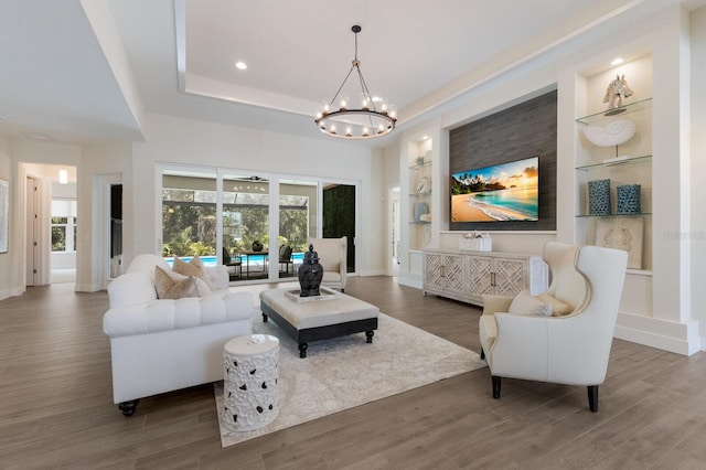 living room with a raised ceiling, built in features, dark hardwood / wood-style floors, and a notable chandelier