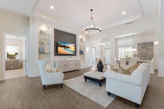 living room with a chandelier, wood-type flooring, built in features, and a raised ceiling