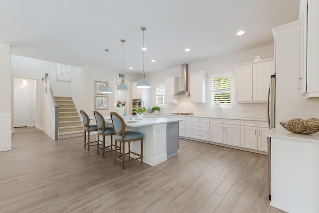 kitchen featuring a center island, wall chimney exhaust hood, pendant lighting, white cabinets, and light wood-type flooring