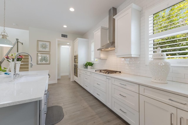 kitchen featuring wall chimney exhaust hood, sink, decorative light fixtures, white cabinets, and light hardwood / wood-style floors