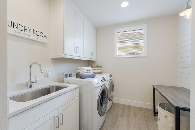 clothes washing area featuring cabinets, sink, washer and dryer, and light hardwood / wood-style flooring