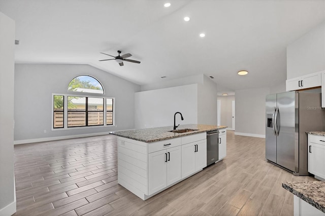 kitchen with stainless steel appliances, open floor plan, a kitchen island with sink, white cabinets, and a sink